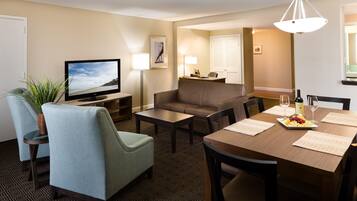 Habitación de hotel con televisor, zona de estar, mesa de comedor y una lámpara.