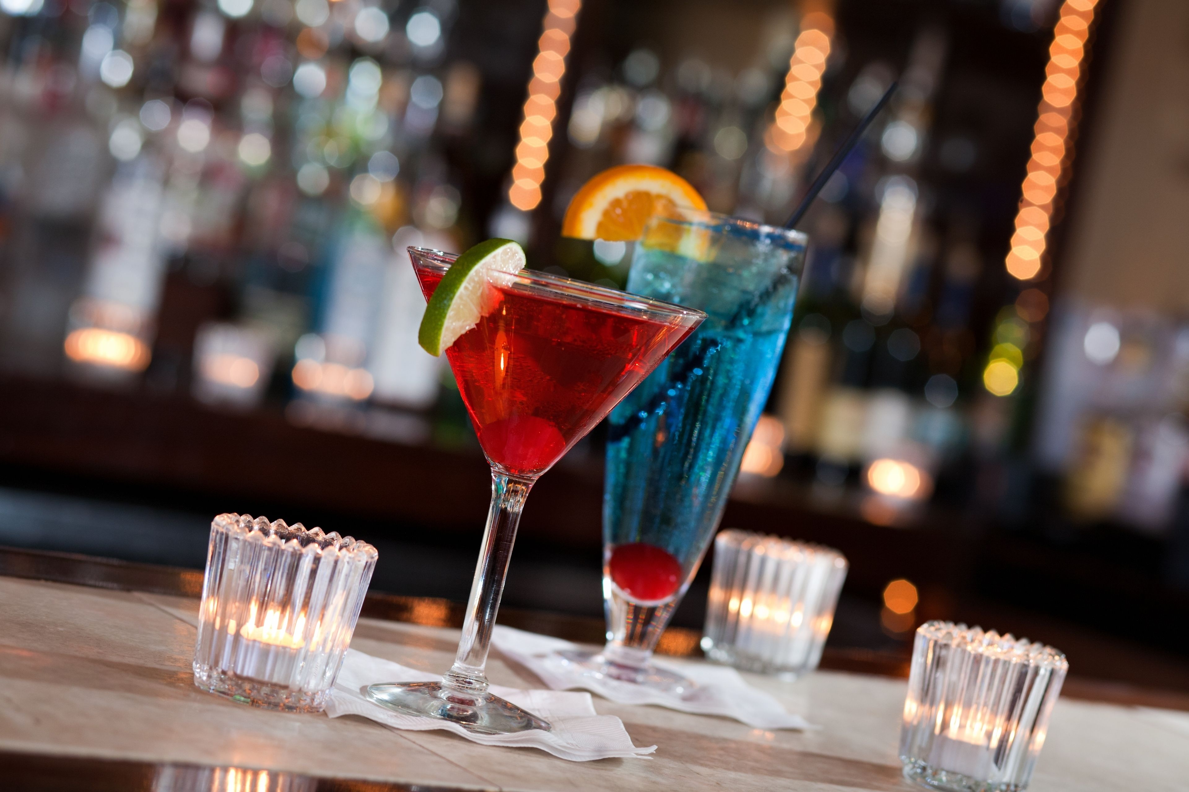 Un bar con dos bebidas, una roja y una azul, cada una adornada con una rodaja de fruta y un gajo de lima.