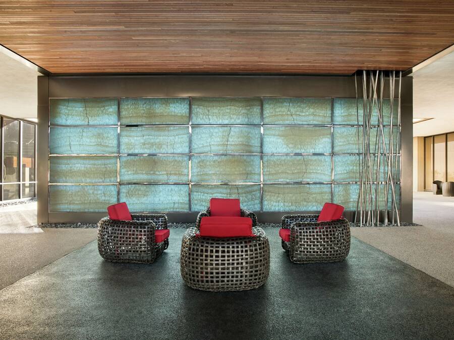 A modern lobby with three wicker chairs with red cushions, a large glass wall, and a wooden ceiling.