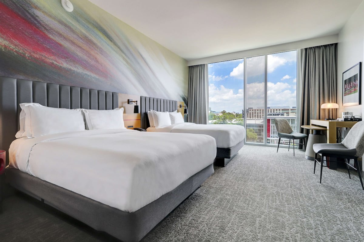 A hotel room with two beds, a desk, and a chair.
