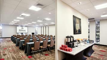 A conference room with rows of tables and chairs, a buffet table with food and drinks, and a Hilton University of Houston sign.