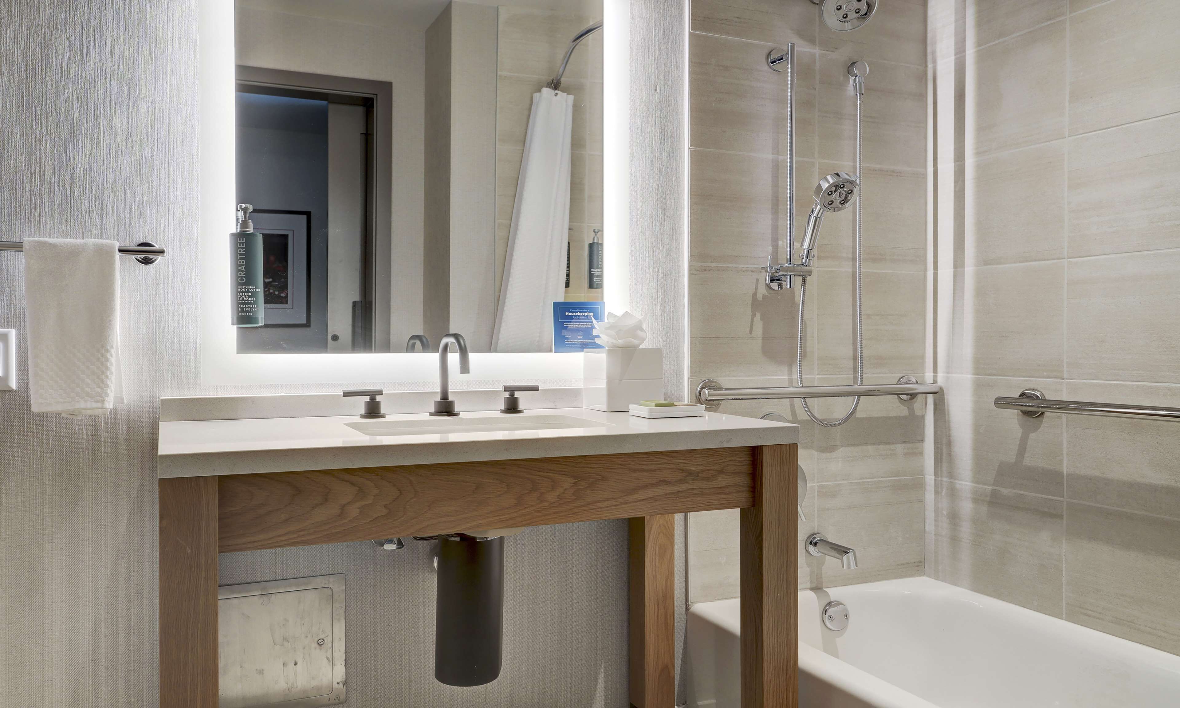 Een moderne badkamer met een houten wastafelmeubel, een grote spiegel, een bad en een douche met een handdouche.