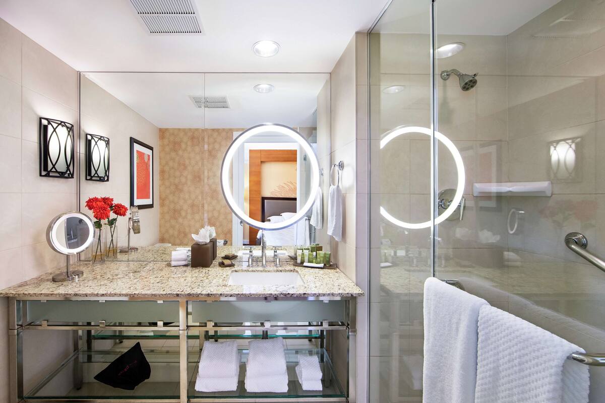 A modern bathroom with a glass shower enclosure, a vanity with a granite countertop, and multiple mirrors.