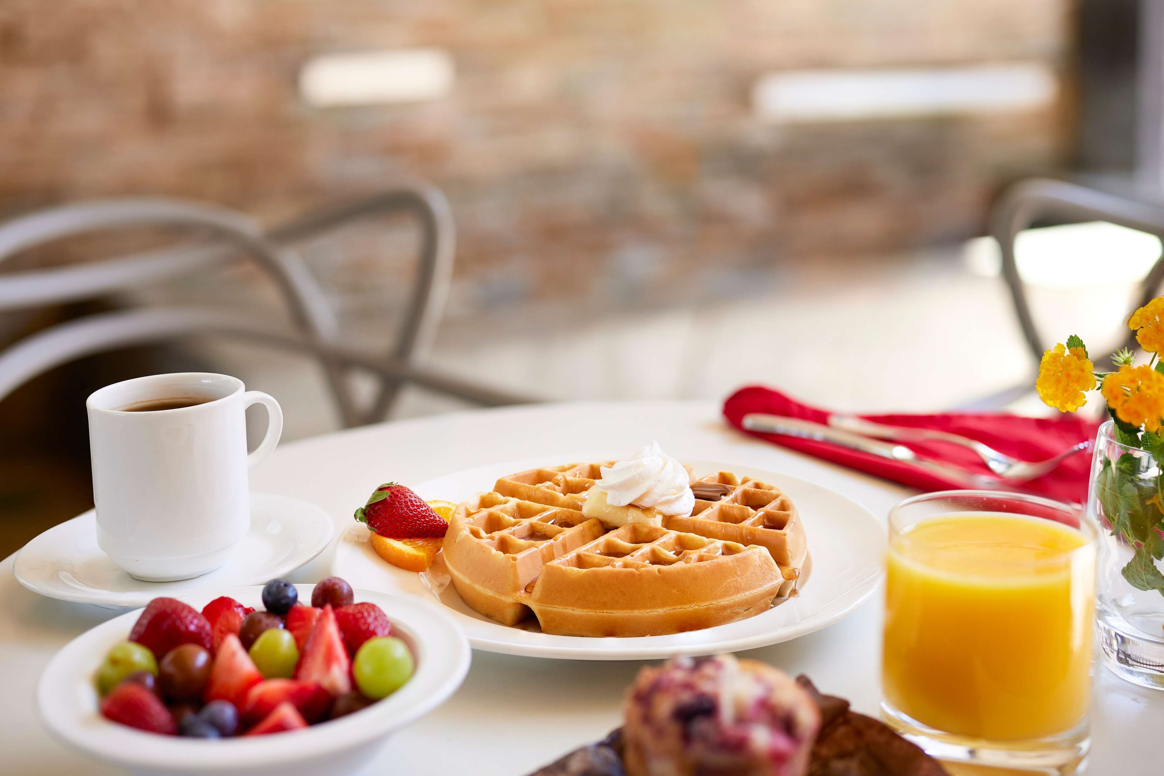 A breakfast setting with waffles, fruit, coffee, and orange juice on a table.