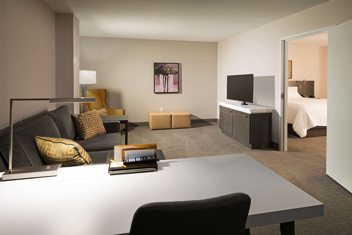 Habitación de hotel con cama, escritorio con computadora portátil, televisor, sofá y un cuadro en la pared.