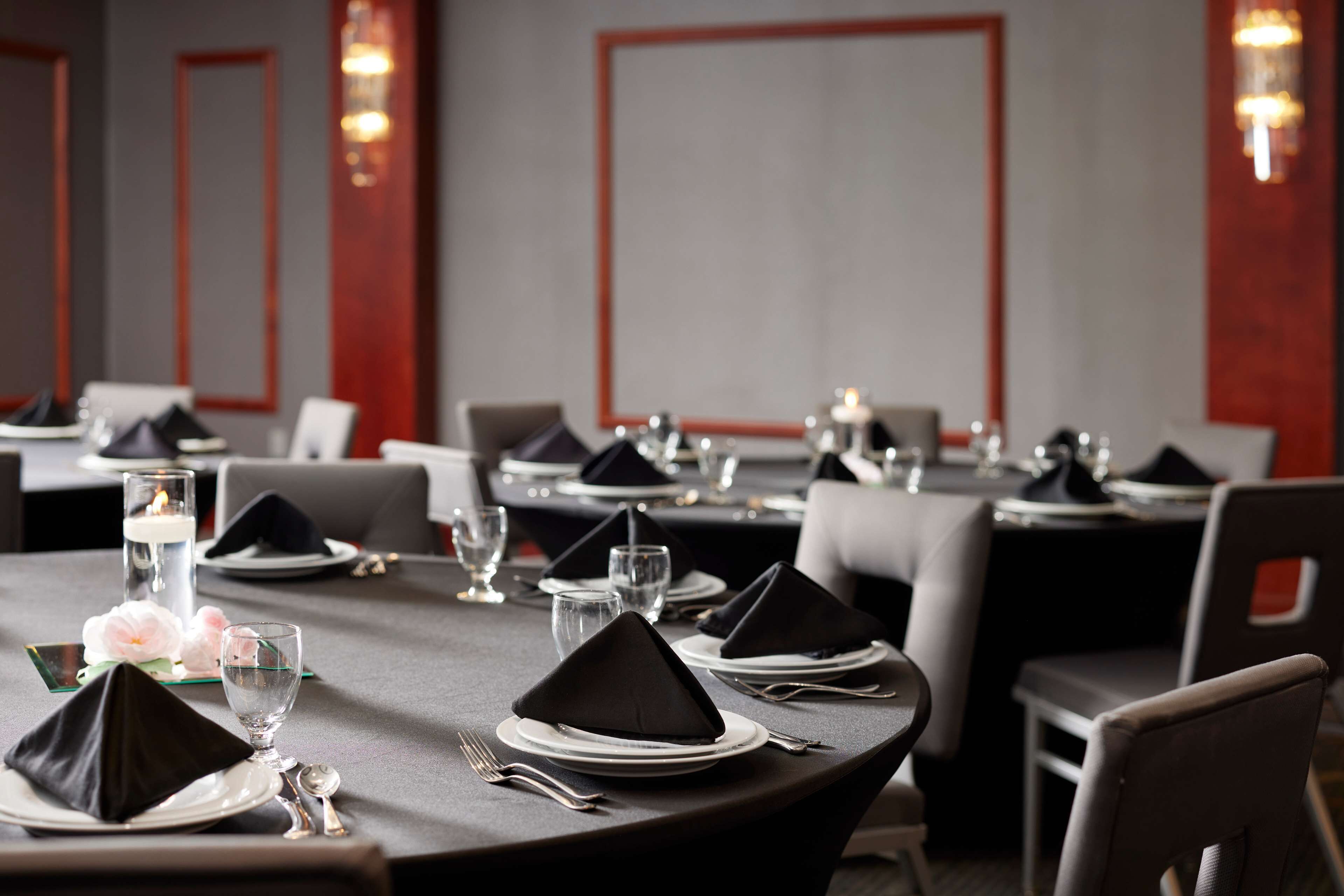 A dining area with tables set for service, featuring black napkins, white plates, and clear glasses.