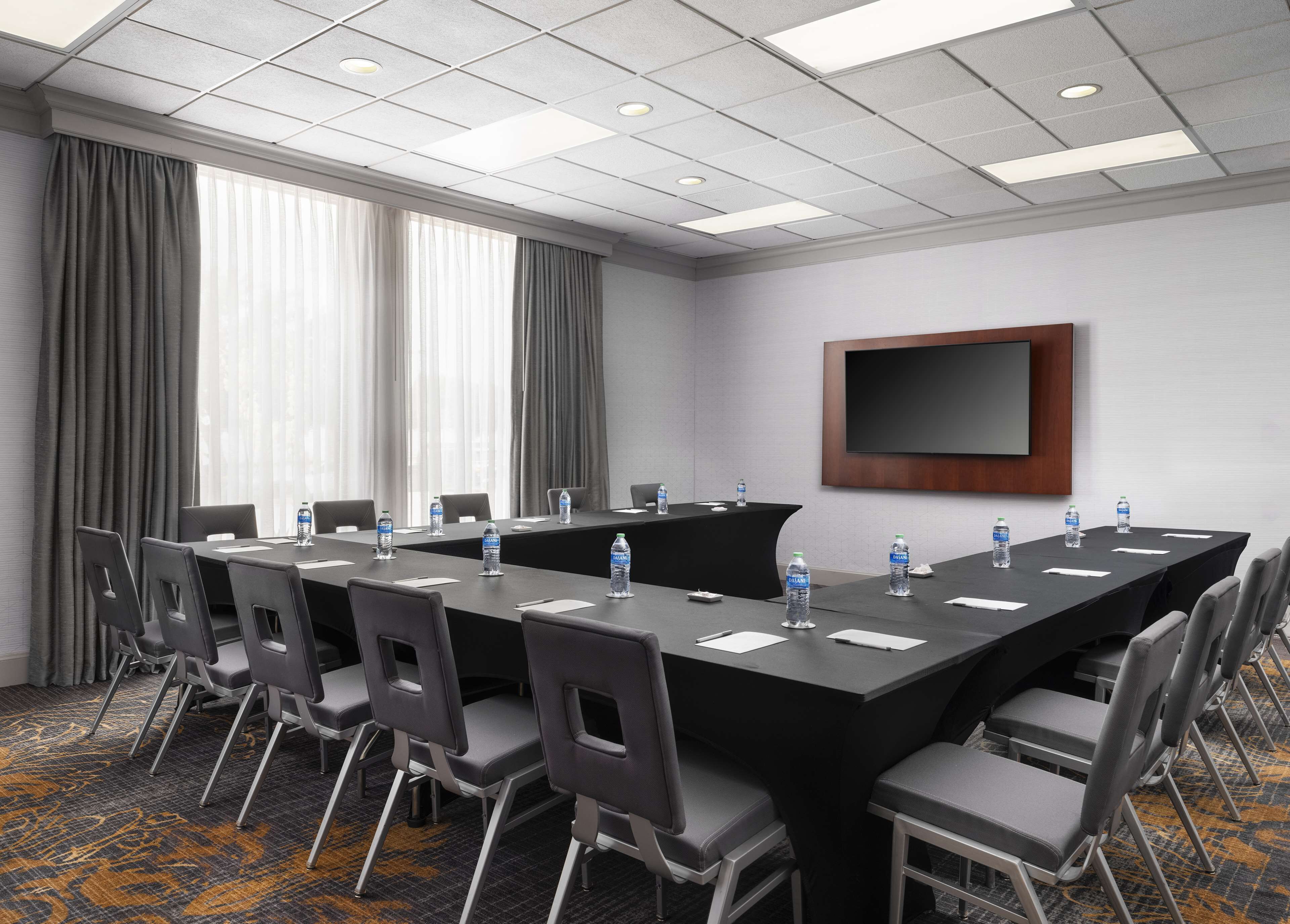 A conference room with a long table, chairs, water bottles, and a flat-screen TV on the wall.