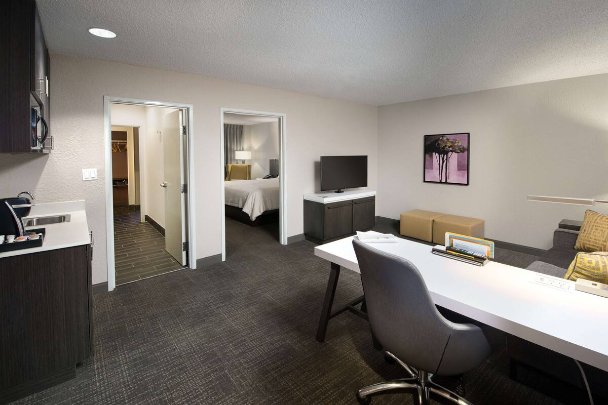 Una habitación de hotel con escritorio, silla, televisor y una cama en la habitación contigua.