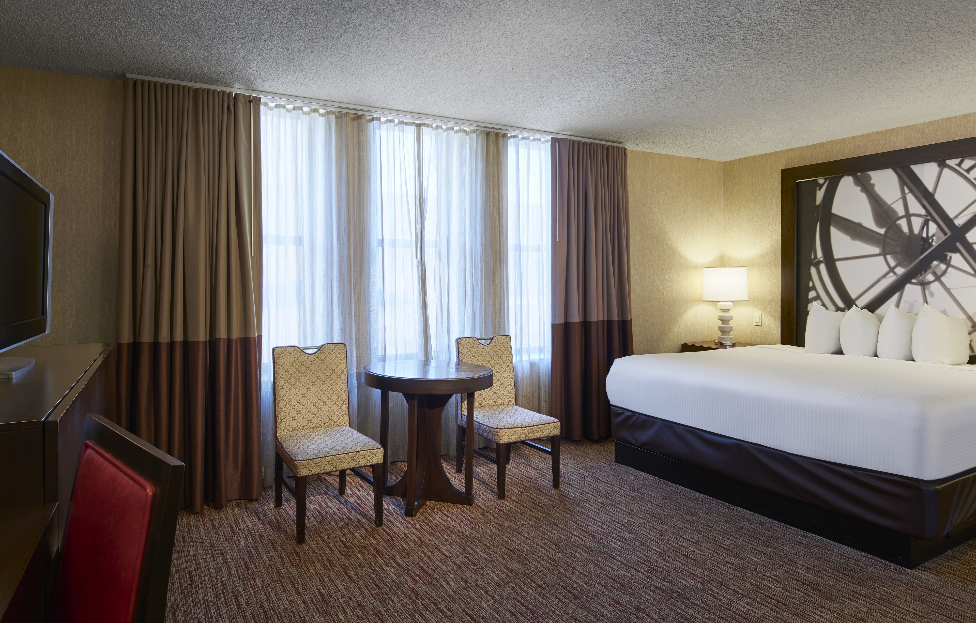 A hotel room with a bed, two chairs, a small table, a TV, and curtains.