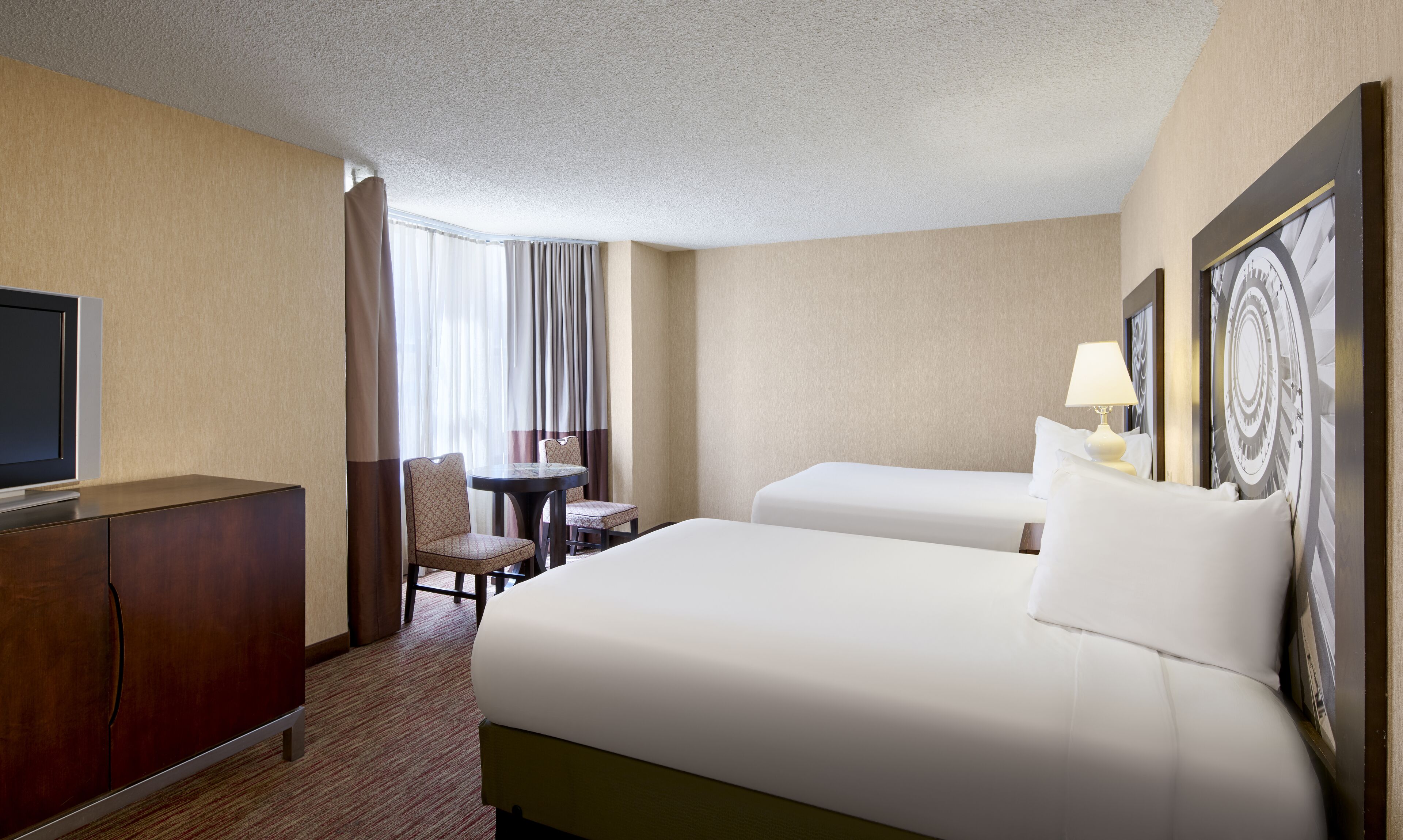A hotel room with a bed, a desk, a chair, a television, and a painting on the wall.