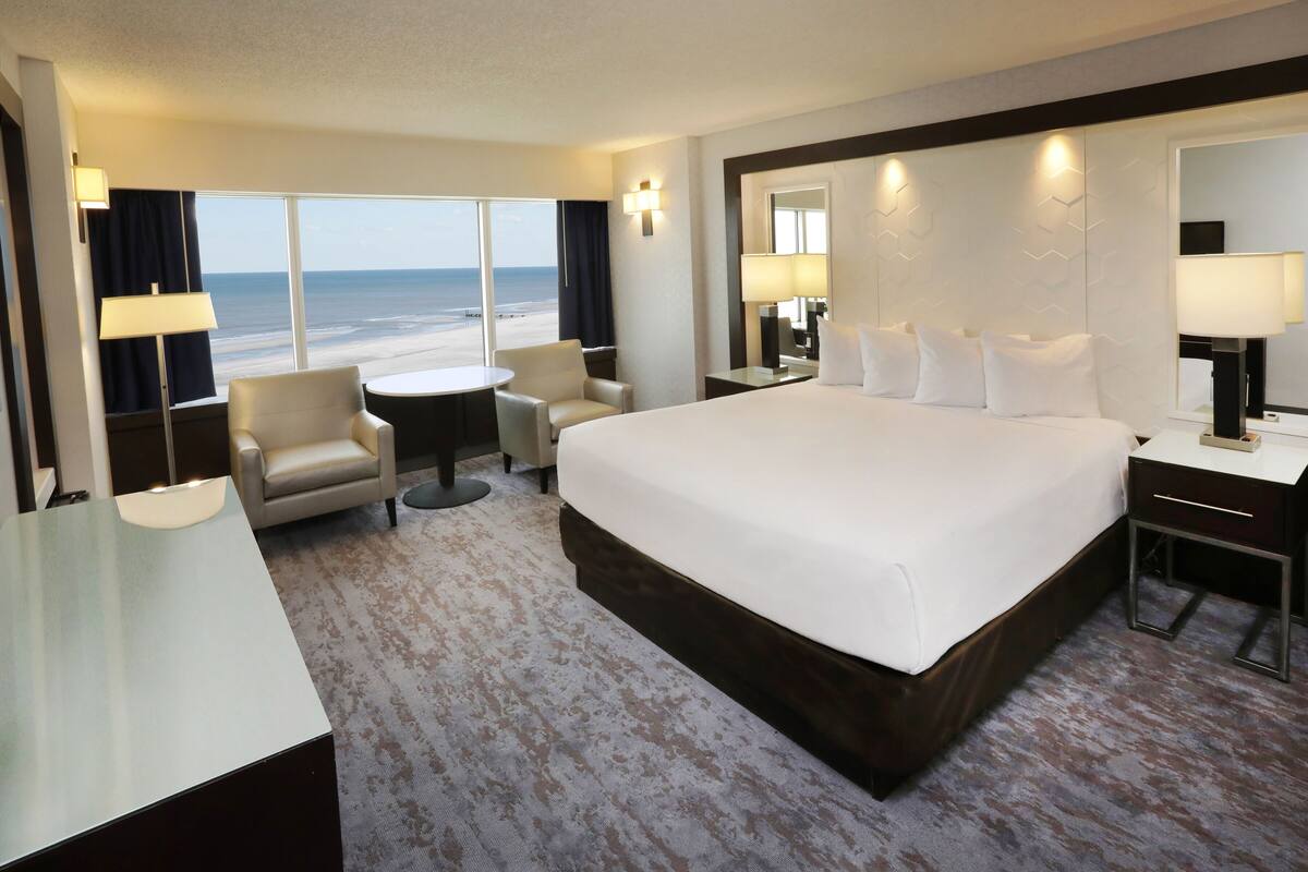 Une chambre d’hôtel avec un grand lit, un bureau, une chaise, une petite table et une vue sur la plage.
