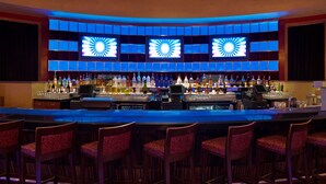 A bar area with a long counter, multiple bar stools, and a wall with illuminated panels.