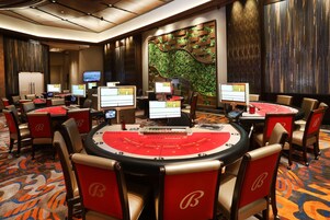Zona de casino con múltiples mesas de blackjack, sillas y monitores mostrando interfaces de juego.