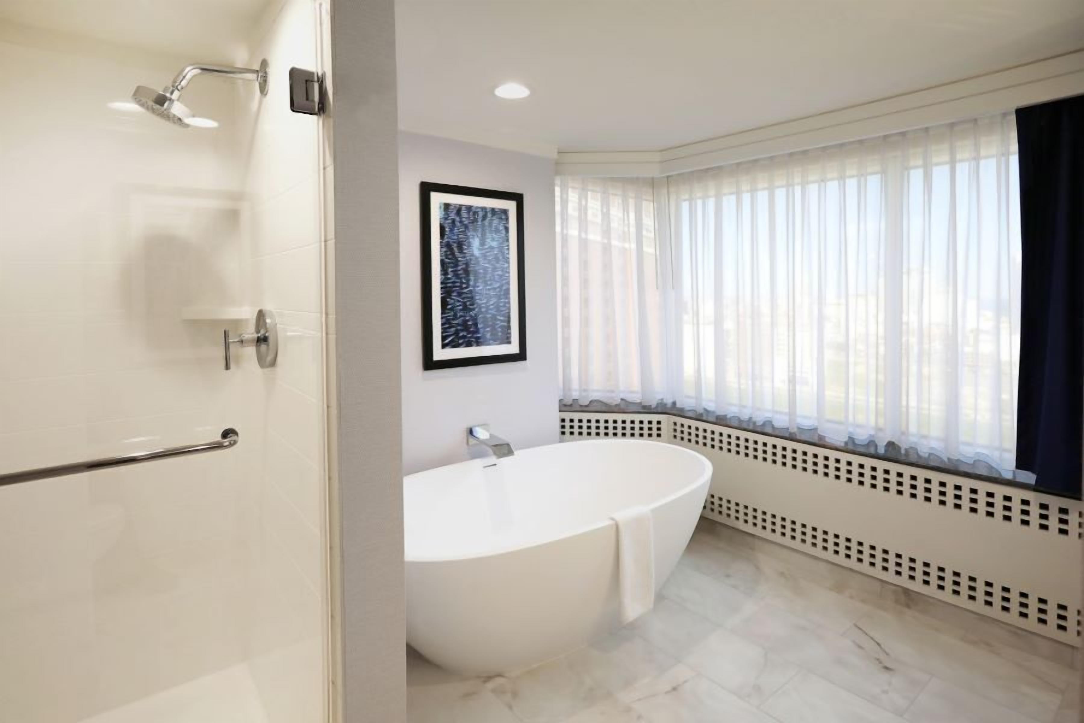 Une salle de bain moderne avec une baignoire sur pieds, une douche et une fenêtre ornée de rideaux légers.