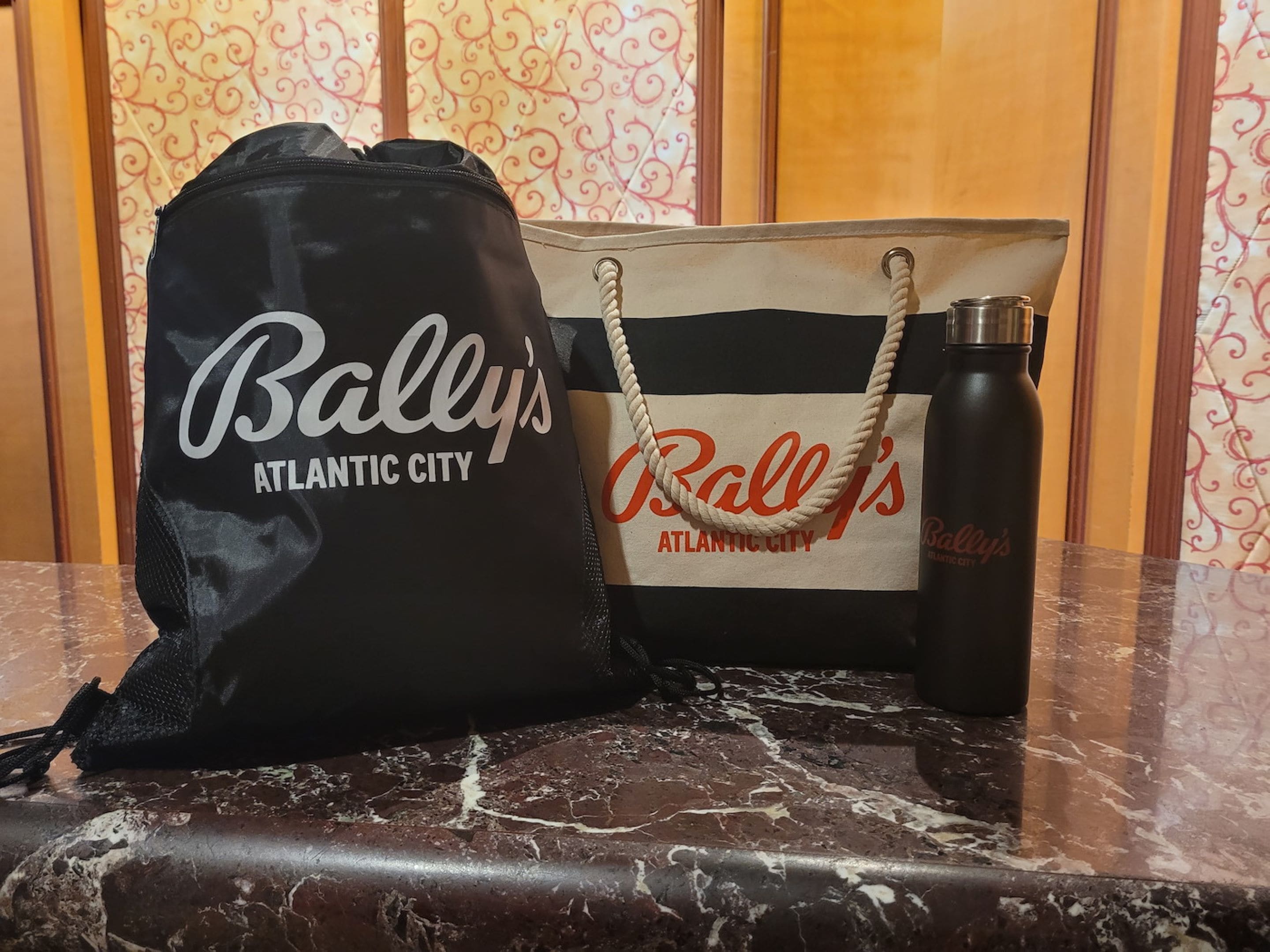 Dos bolsos de mano, uno negro y otro beige, con la inscripción "Bally's Atlantic City", sobre una superficie de mármol.