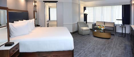 A hotel room with a large bed, a seating area with a sofa and armchairs, a small coffee table, and a TV.