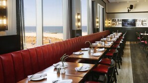 A restaurant with a long counter, red cushioned booths, and large windows offering a view of the beach.