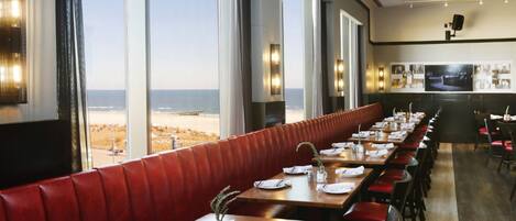A restaurant with a long counter, red cushioned booths, and large windows offering a view of the beach.