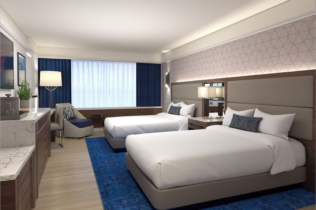 Une chambre d’hôtel avec deux lits, un bureau, une chaise, une lampe et une grande fenêtre avec des rideaux.