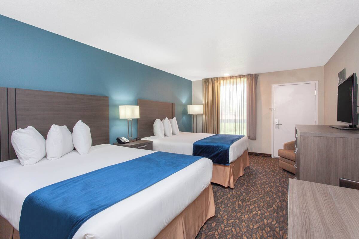 A hotel room with two beds, a desk, a television, and a door.