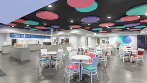 A modern cafe with white tables and chairs, a counter with a menu, and a colorful ceiling. - Grand Hotel Orlando at Universal Blvd - Shuttle to Theme Parks (Orlando)