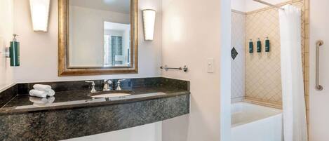 A bathroom with a granite countertop, a large mirror, two wall-mounted lights, a bathtub, and a shower with a glass door.