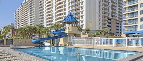 A swimming pool with a blue slide and lounge chairs, surrounded by tall residential buildings.