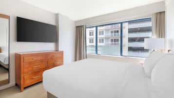 A hotel room with a large bed, a wooden dresser, a flat-screen TV, and a large window with a view of a building.