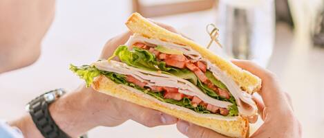 A person holding a sandwich with visible layers of lettuce, tomato, and meat.