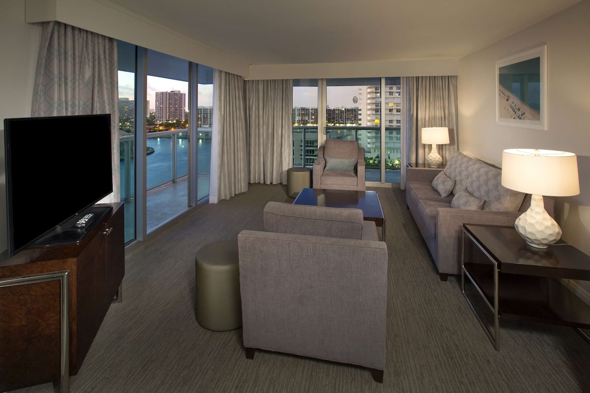 Ein modernes Hotelzimmer mit großem Fernseher, bequemen Sitzgelegenheiten, einem kleinen Tisch und Blick auf die Stadt.