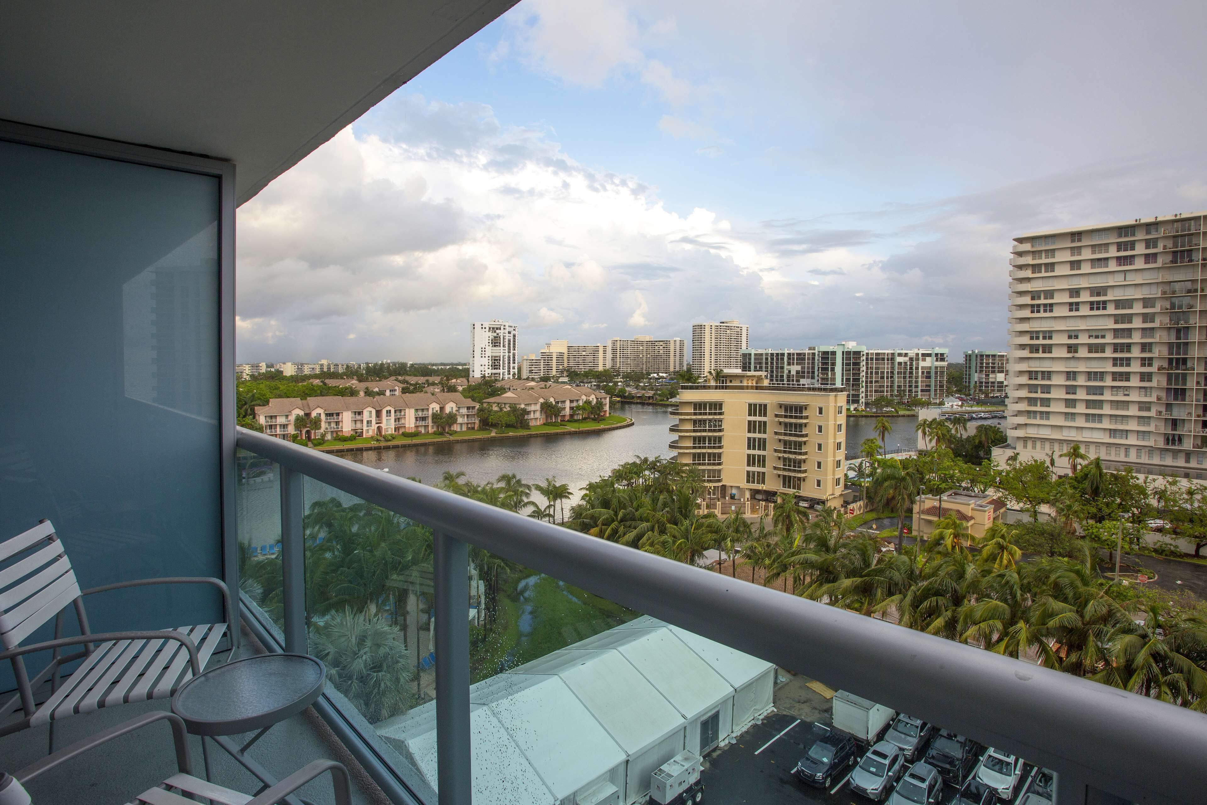 A balcony with a view of a river, palm trees, and high-rise buildings.