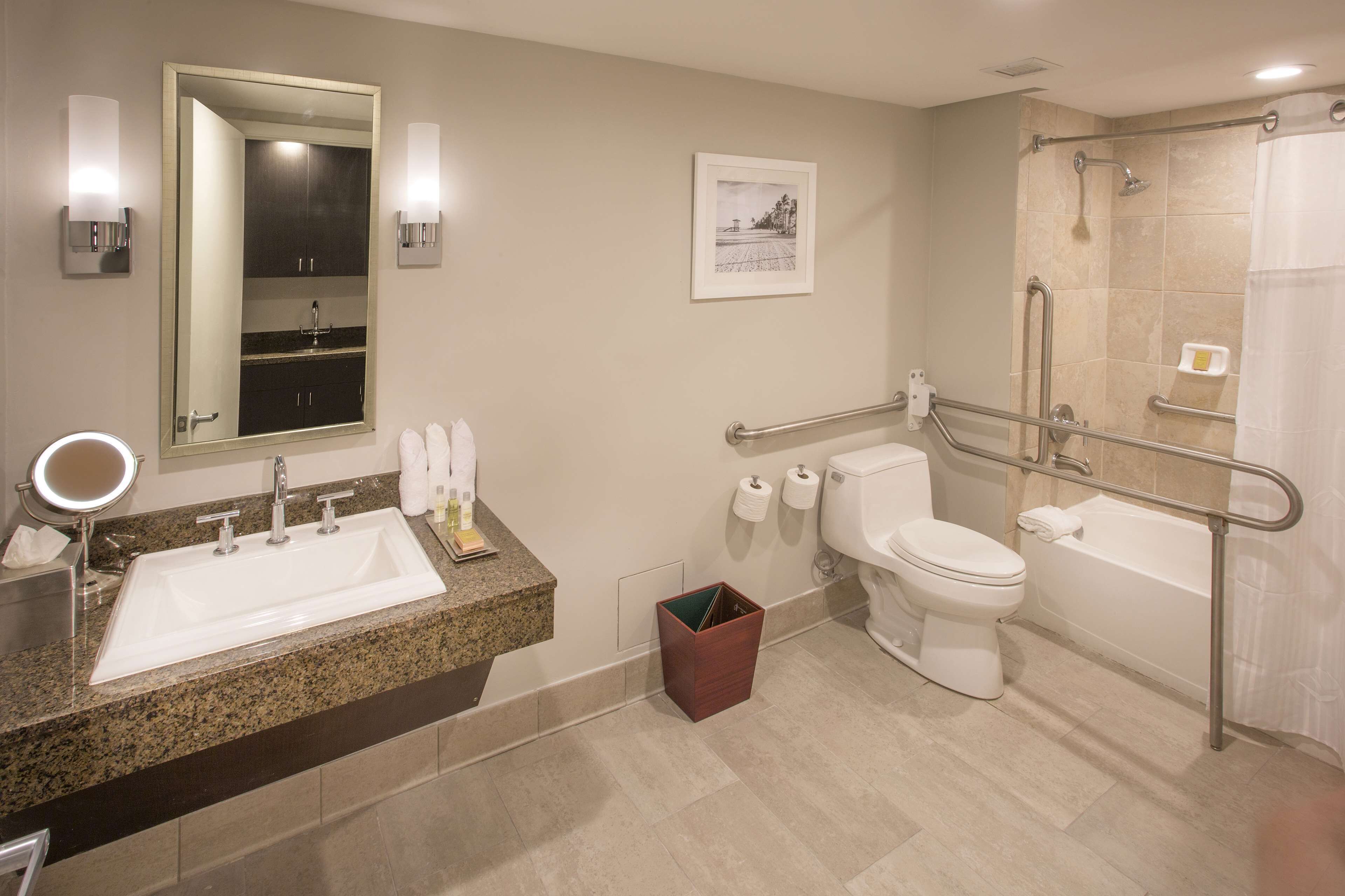 A modern bathroom with a sink, toilet, and bathtub. It includes a mirror, towel rack, and hand soap.
