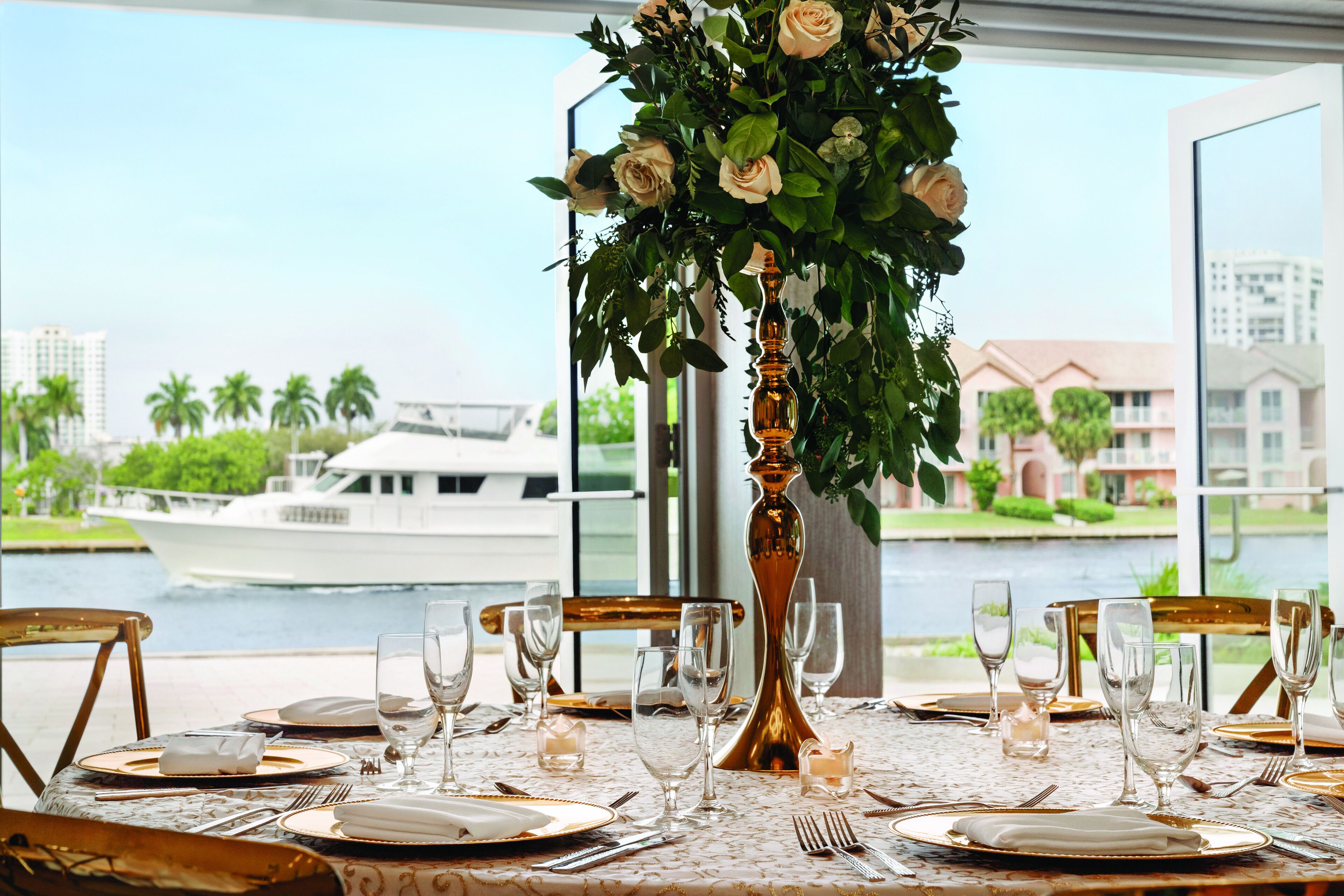 A table set for a meal with a view of a river and a boat in the background.