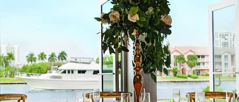 Una mesa lista para una comida con vistas a un río y un barco al fondo.