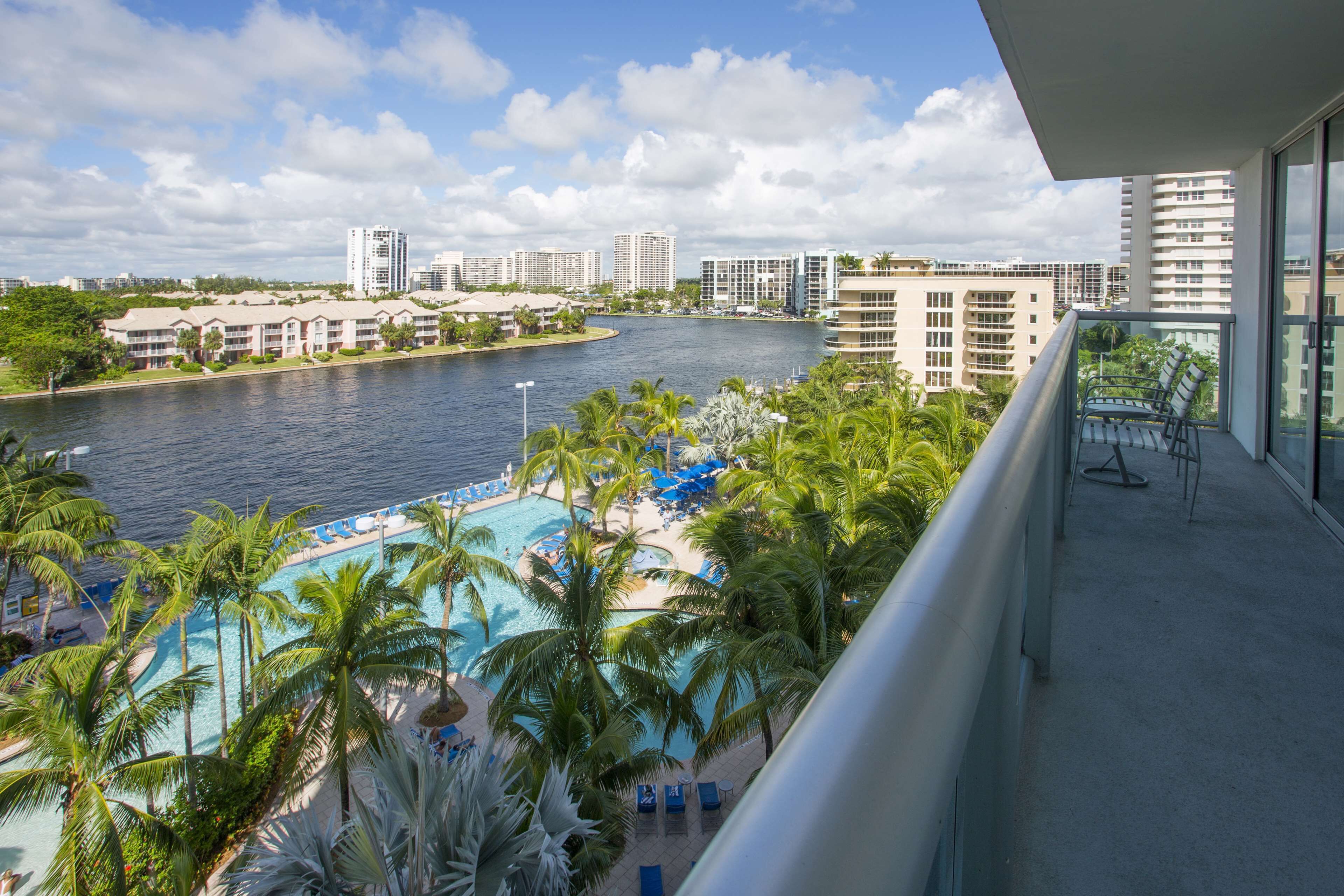 A hotel balcony with a view of a swimming pool, palm trees, and a river.