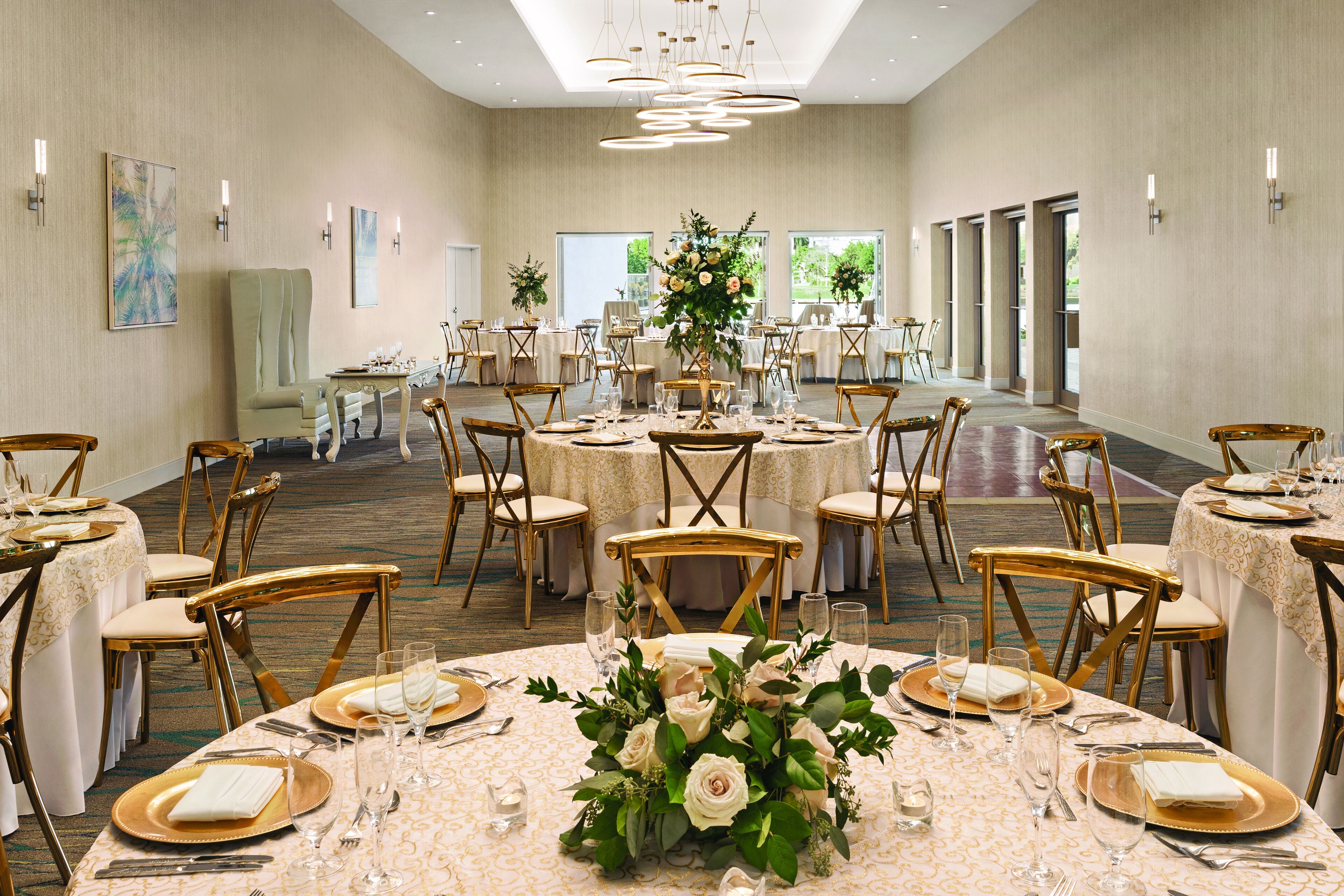 A banquet hall with round tables set for dining, featuring gold and white tablecloths, gold chairs, and floral centerpieces.