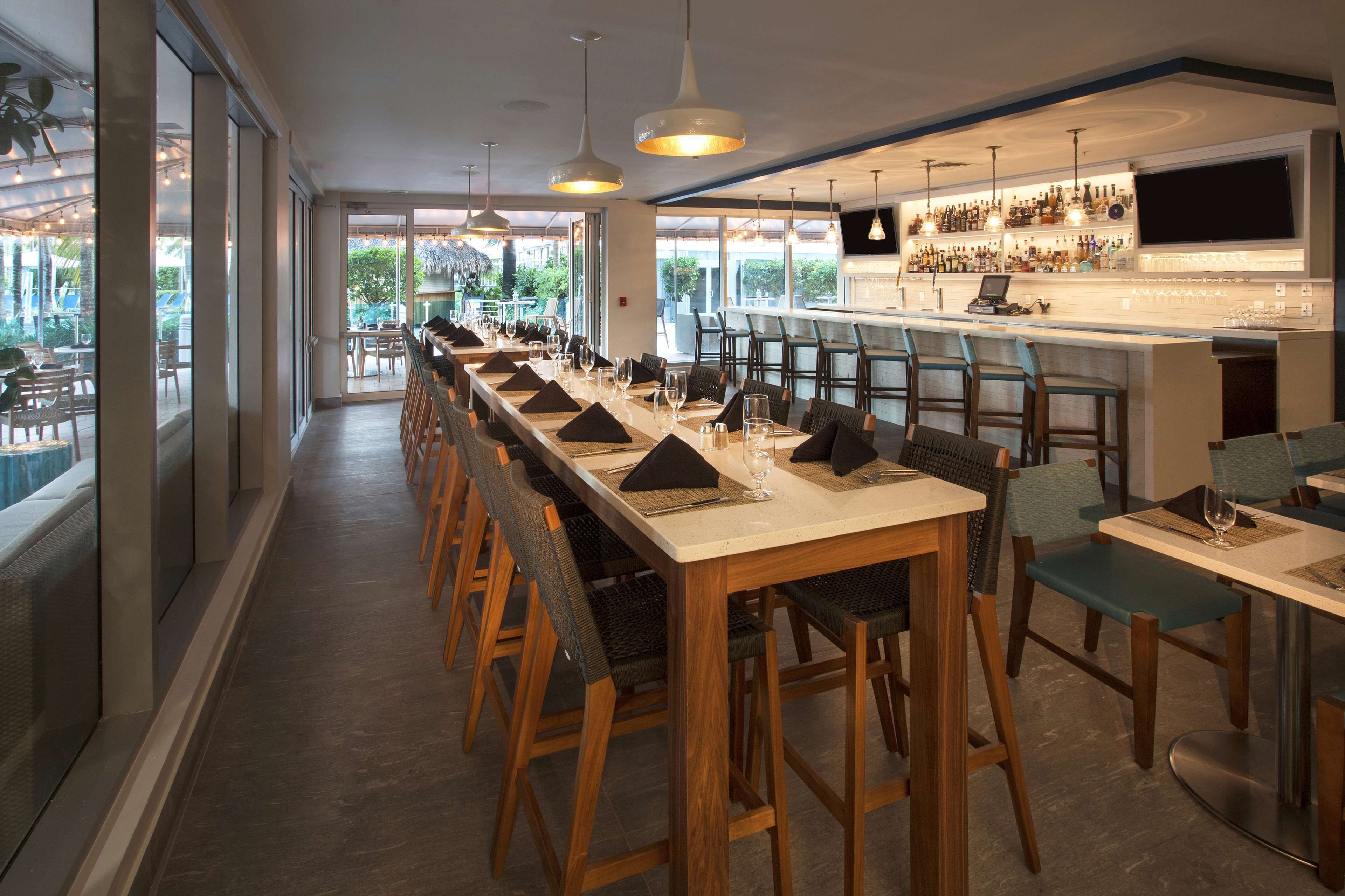 A long dining table with chairs, a bar area with a TV, and large windows offering a view.