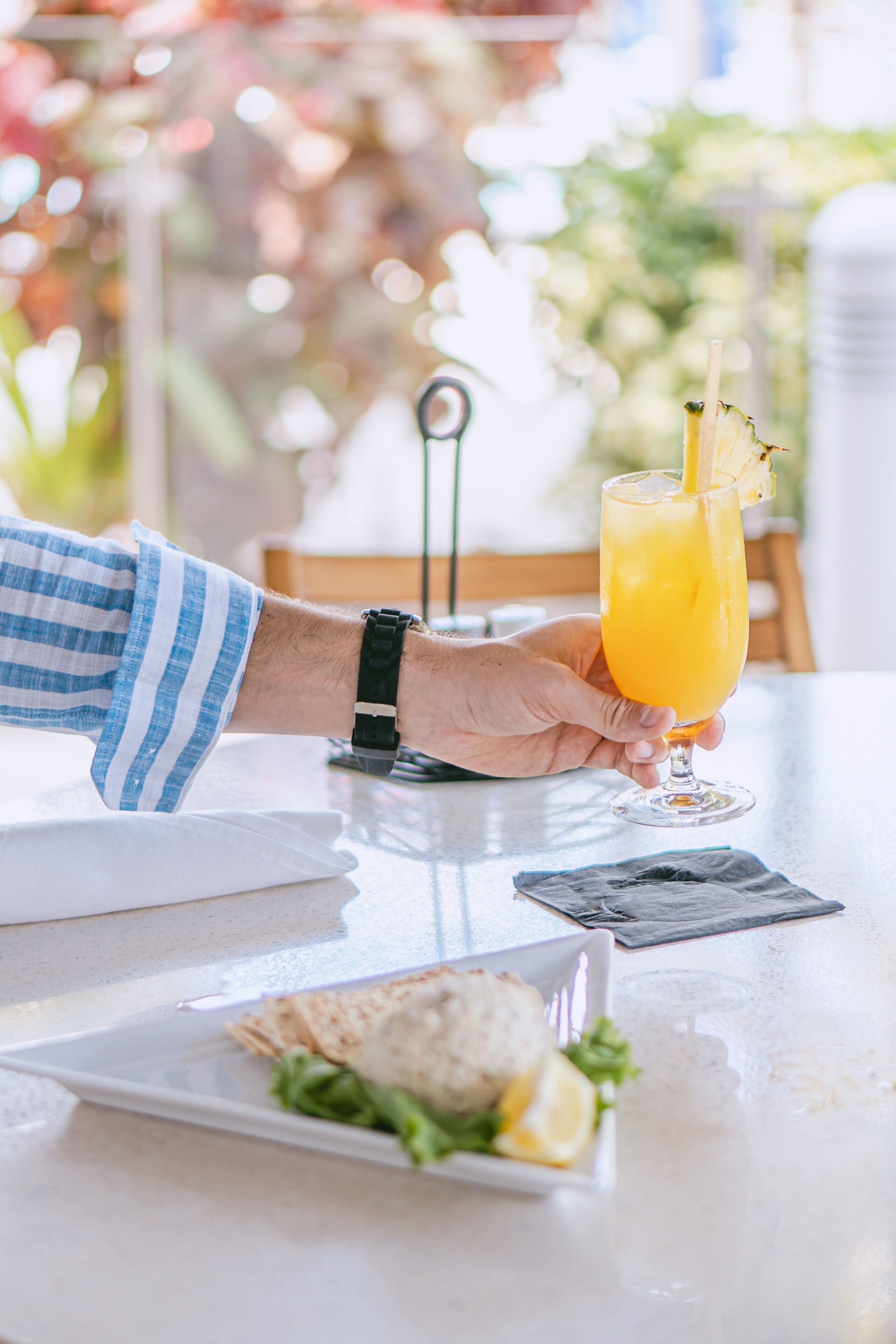 Una persona sosteniendo un vaso de jugo de naranja con una pajita, una servilleta y un plato con comida sobre una mesa.