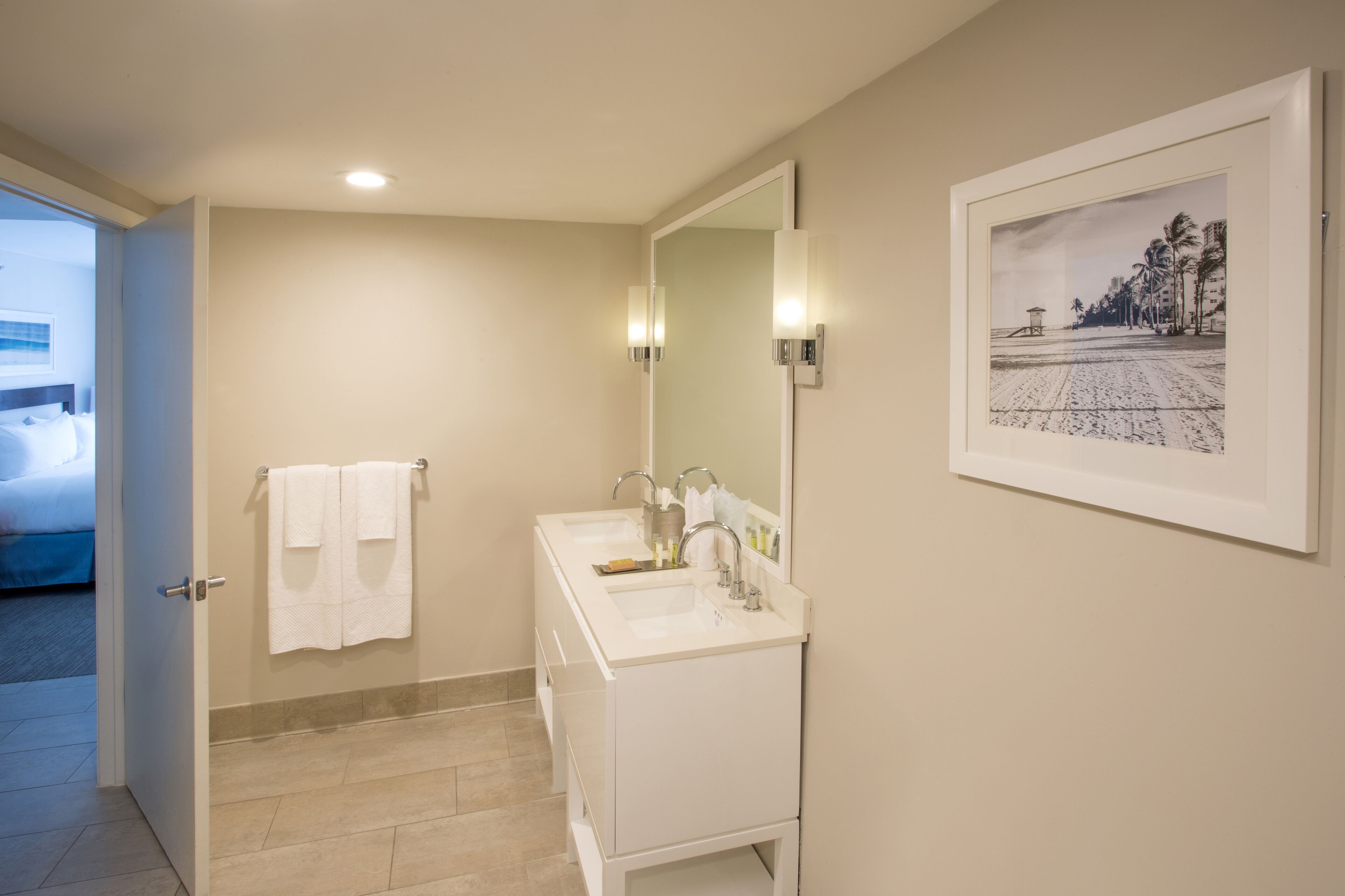 A bathroom with a double sink, a large mirror, and a framed picture on the wall.