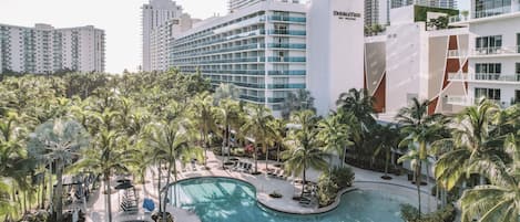 Hotel com piscina rodeada por palmeiras e espreguiçadeiras.