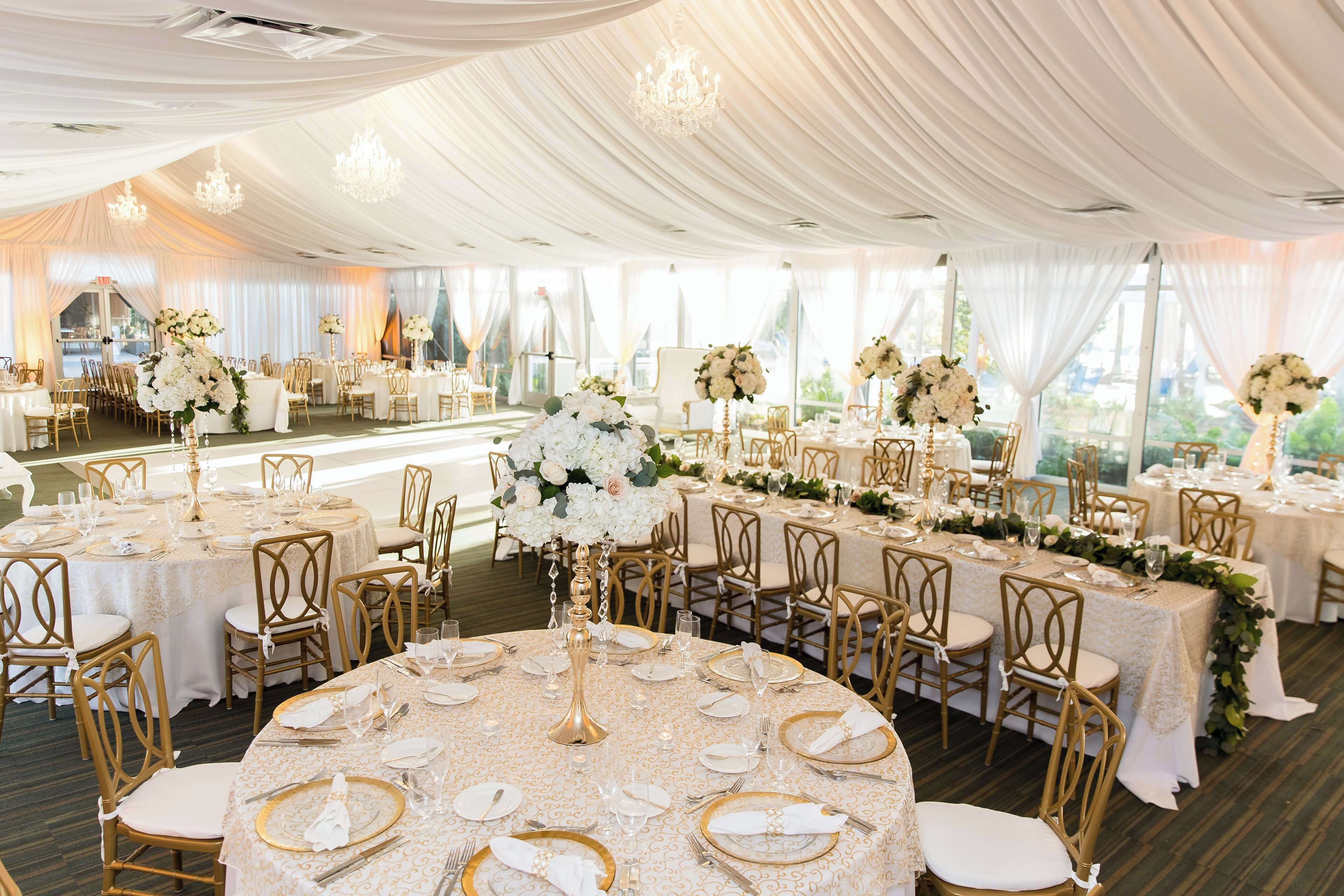 A banquet hall with round tables set for a formal event, featuring gold chairs and white tablecloths.