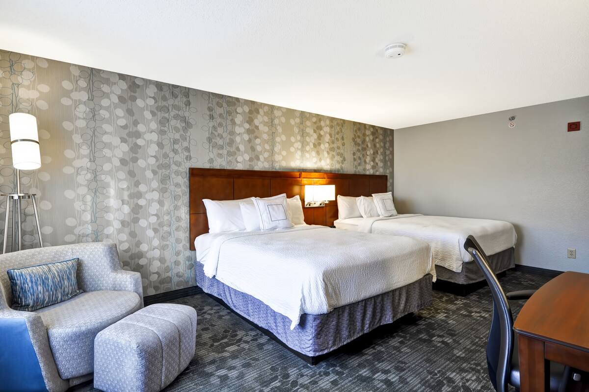 Ein Hotelzimmer mit zwei Betten, einer Schlafcouch, einem Schreibtisch und einem Wandteppich mit Muster.