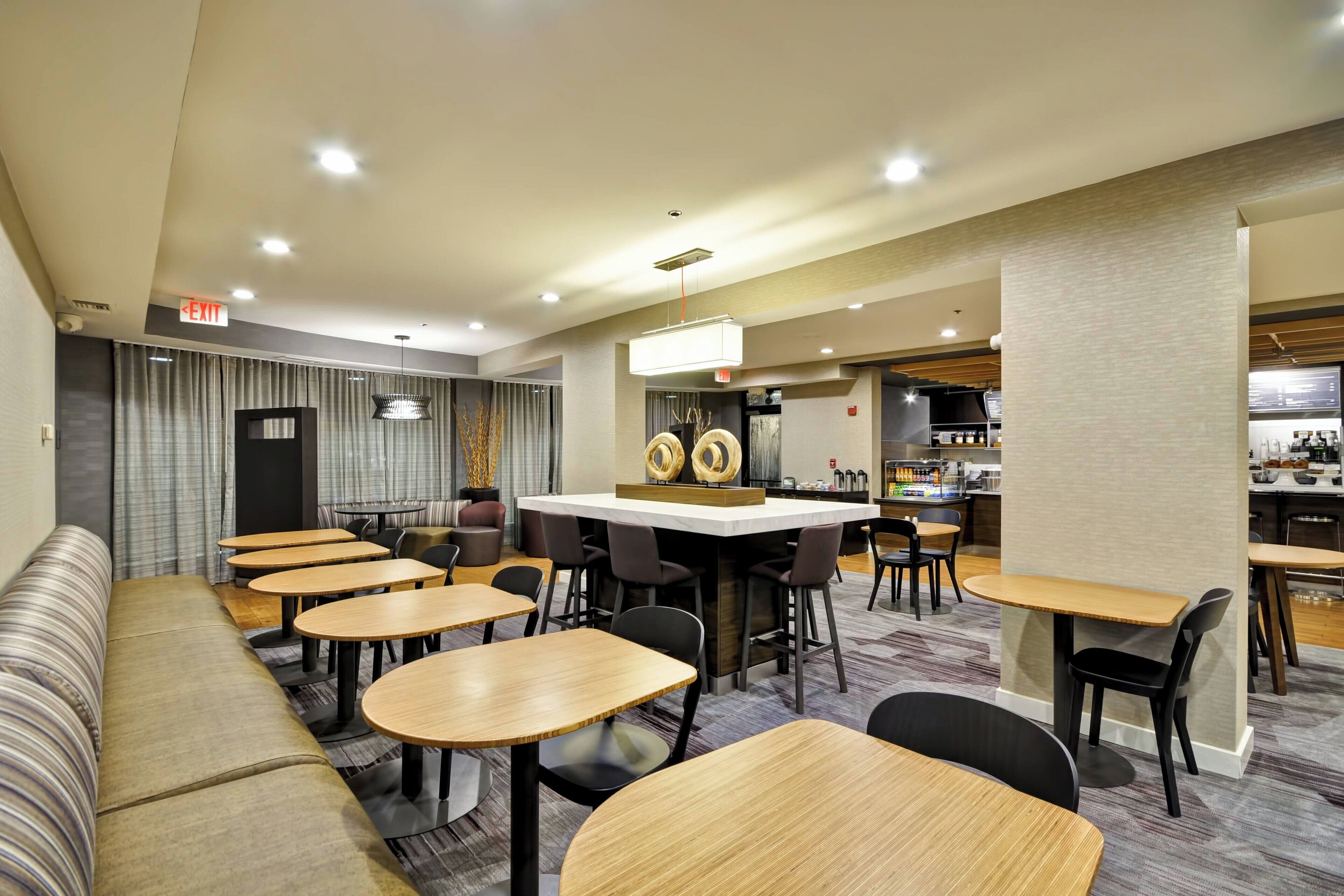 Un restaurante moderno con varias zonas de estar, que incluyen un bar y un comedor con mesas y sillas redondas.