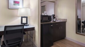 Een compacte hotelkamer met kitchenette, bureau met stoel, magnetron, koelkast en koffiezetapparaat.