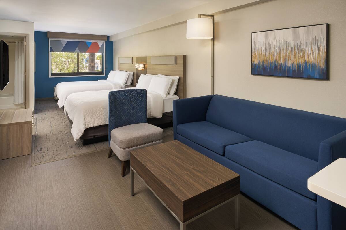 Ein Hotelzimmer mit zwei Betten, einem blauen Sofa, einem Holztisch und einem Bild an der Wand.