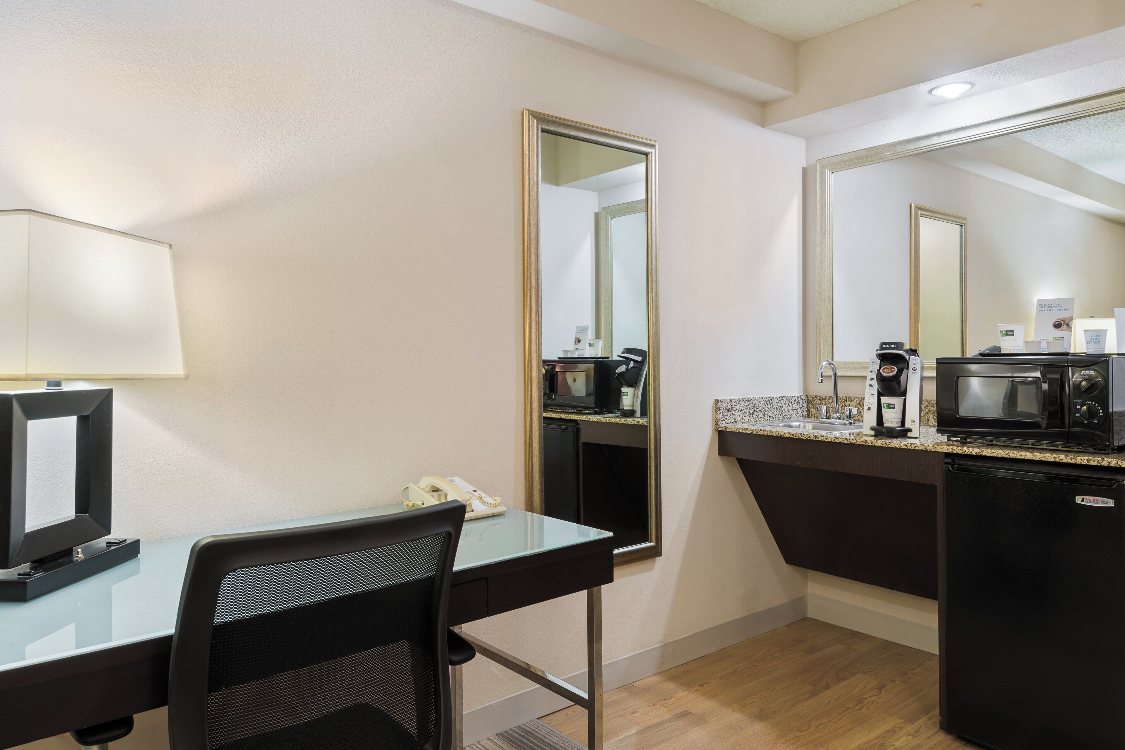 A hotel room with a desk, chair, and kitchenette.