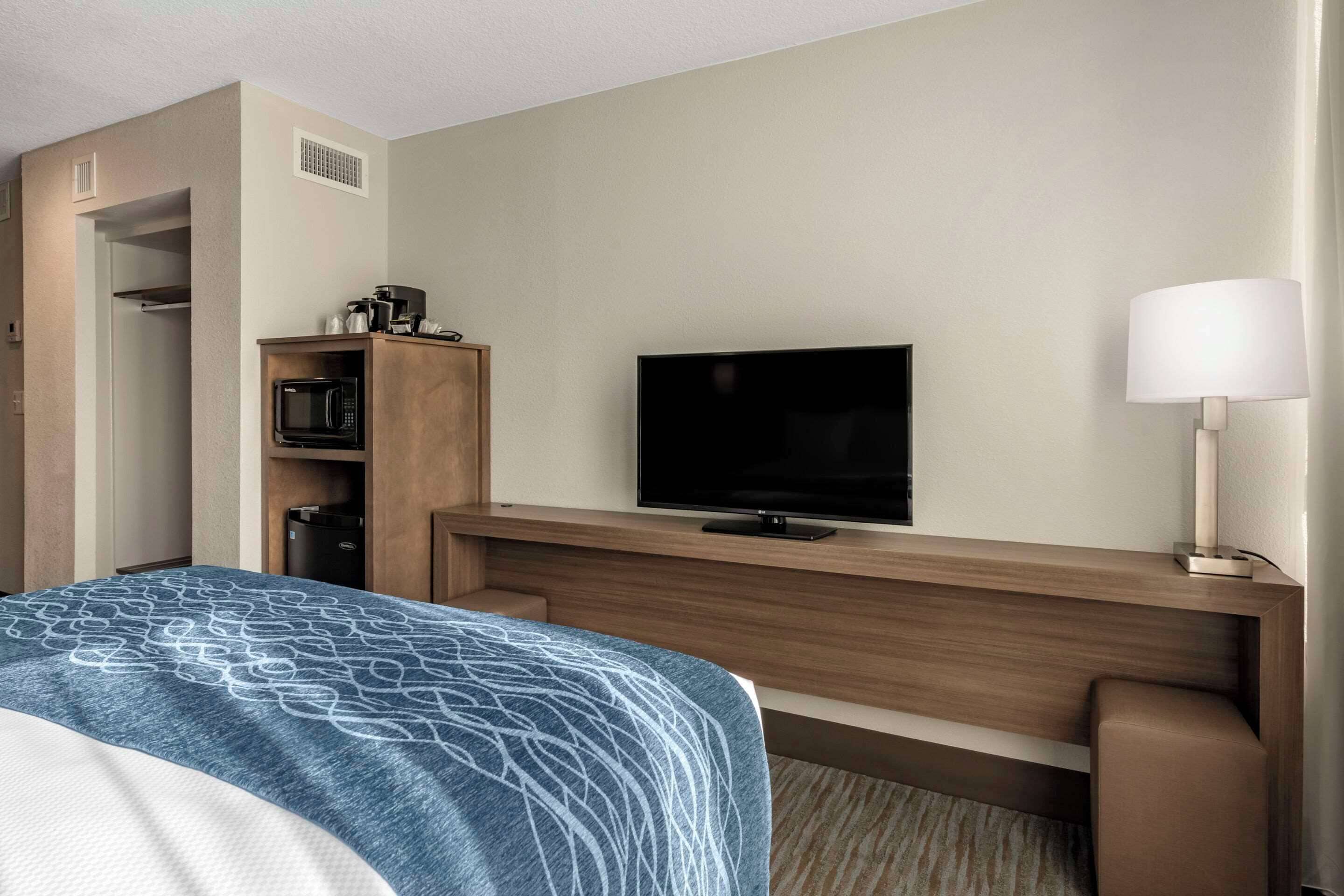 A hotel room with a bed, a television, a desk with a lamp, a microwave, and a coffee maker.