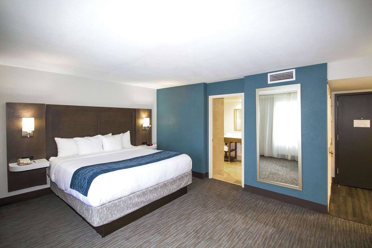 Habitació d'hotel amb un llit gran, una taula de nit amb un telèfon, una làmpada penjada a la paret i una porta que dóna a un bany.