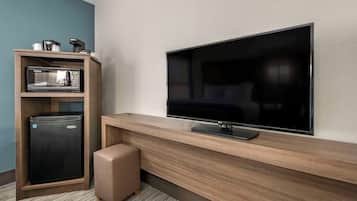 A modern hotel room with a flat-screen TV mounted on the wall, a minibar, and a small seating area.
