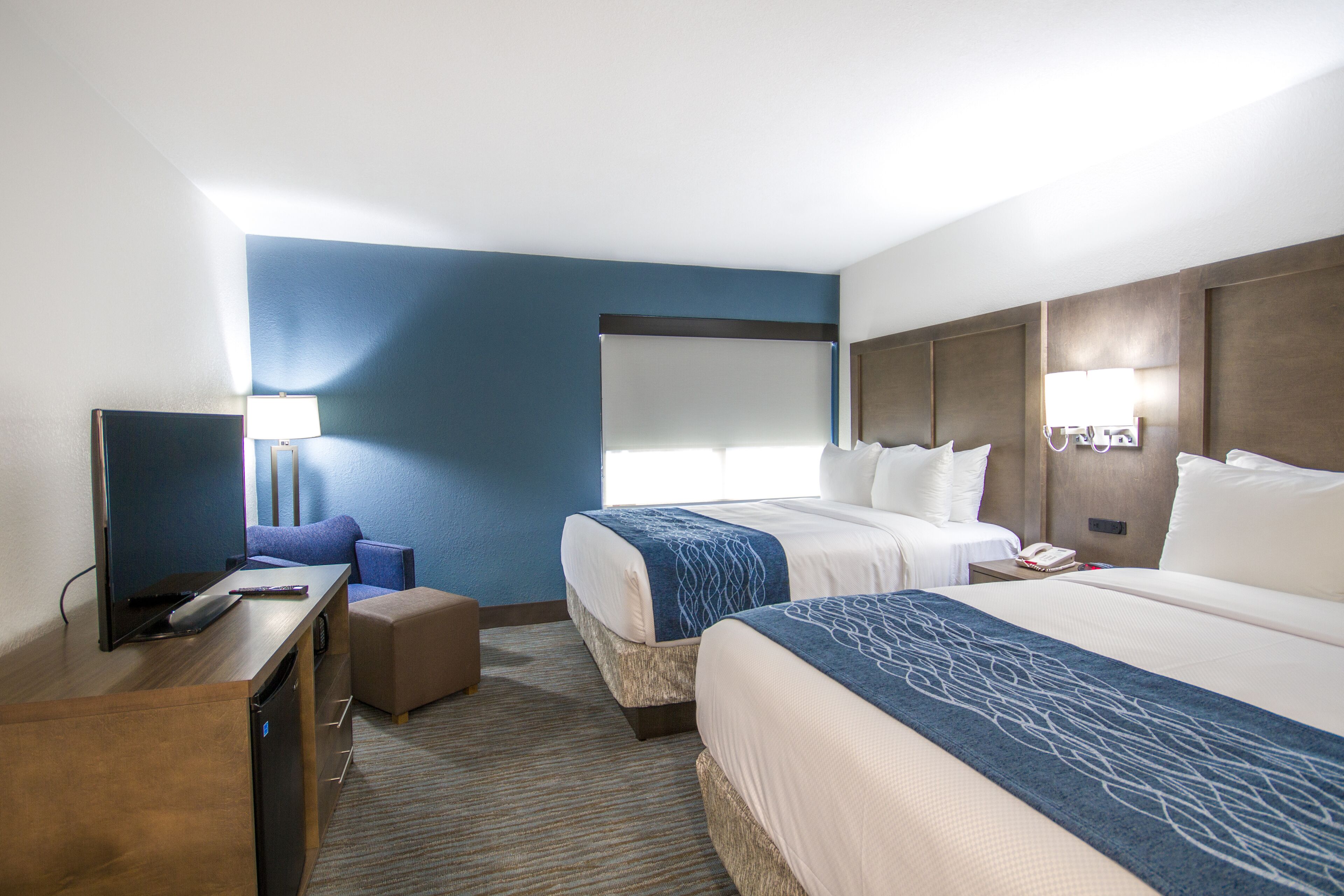 A hotel room with two beds, a desk with a TV, a lamp, and a window.